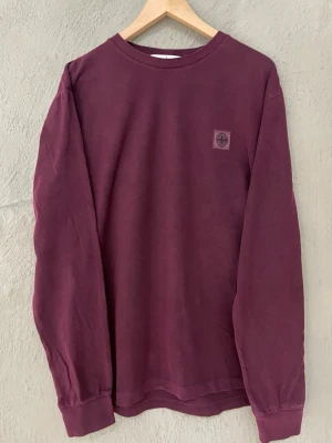 Vinröd långärmad tröja Stone Island - Vinröd långärmad tröja från Stone Island med diskret logga på bröstet. Tröjan passar M/L.