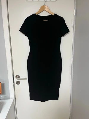 Svart tight kortärmad klänning - En stilren svart klänning med tight passform och korta ärmar. Klänningen har en enkel, klassisk design utan synliga detaljer och är knälång. Perfekt för dig som gillar minimalistisk stil. Står ej storlek men passar M/L. Sitter hyfsat tajt.