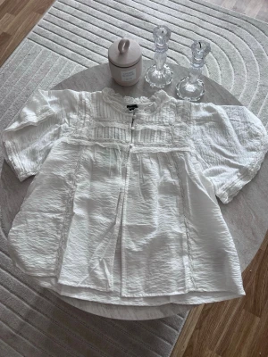 boho blouse  - Söt vit blus från Gina Tricot med korta ärmar, spetsdetaljer och rundad hals. Blusen har en romantisk känsla med dekorativa sömmar och lätt rynkad struktur. Perfekt att styla med jeans eller kjol för en trendig look.