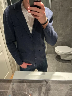 Marinblå stickad kavaj från John Henric - Stilren marinblå kavaj från Massimo Dutti med två knappar framtill och tre utanpåliggande fickor. Kavajen har klassisk krage och är tillverkad i ett mjukt, stickat material som ger en avslappnad men ändå dressad look. Jag på bilden är 188cm och bär storlek M. Hör av er FBIs frågor eller fler bilder:)