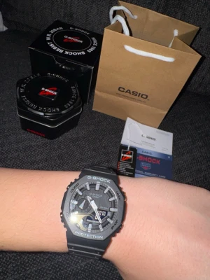 Svart Casio G-Shock klocka - Säljer en svart Casio G-Shock klocka med robust design och digital-analog urtavla. Klockan har tydliga vita detaljer, skyddande boett och svart armband i syntetmaterial. Kommer med originalförpackning, manual. Perfekt för dig som gillar sportig och tålig stil.