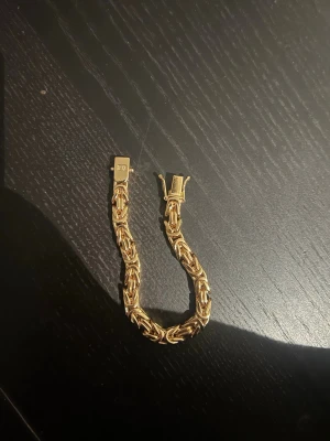 Guldarmband med kedjedesign - Snyggt armband i guldfärgad metall med en robust kedjedesign som ger en exklusiv känsla. Länkarna är tätt sammanlänkade och armbandet har ett smidigt lås. Perfekt för dig som vill ha ett statement-smycke som sticker ut.