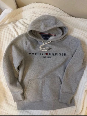 Tommy hilfigher hoodie grå - En grå hoodie som är i bra skick säljer den för att jag inte passar mig aldrig använt för att jag köpte fel storlek en ny sån hoodie kostar över 1000kr