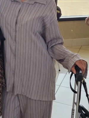 Randig två delad outfit med skjorta och byxa - Säljer en oversized tvådelad outfit (two piece set) i mjukt tyg med tunna vertikala ränder i beige och grått. Setet består av en långärmad skjorta med krage och knappar samt matchande byxor med lös passform. Perfekt för chill dagar hemma. Är i storlek M men passade mig perfekt jag som har storlek S:)