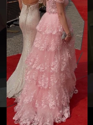 Rosa långklänning med spets och volanger som är Kemtvättad  - KEMTVÄTTAD. Drömmig rosa långklänning med flera lager volanger och vackra spetsdetaljer. Klänningen har offshoulder-band och ett blommigt mönster över hela tyget. Perfekt för bal eller student😍😍 köpt på dress room i Göteborg för 5500 kr. Är i storlek 6/xs men jag som brukar ha s passade den lika bra 