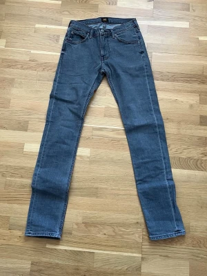 Gråa raka jeans från Lee - Säljer ett par klassiska blå jeans från Lee med rak passform och fem fickor. Jeansen har normal midja och är tillverkade i slitstarkt denimtyg. Perfekta för dig som gillar en tidlös och enkel stil. Storlek 27 32, använda fåtal gånger syns inte alls på dem.