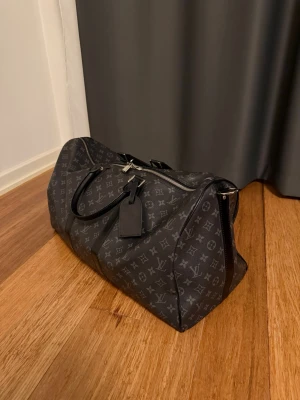 Louis Vuitton svart monogram weekendbag - Stilren och rymlig resväska från Louis Vuitton i svart canvas med monogrammönster. Väskan har dubbla handtag i läder, silverfärgade metalldetaljer och dragkedja upptill. Perfekt för dig som vill resa med stil och ha plats för allt du behöver. Axelremmen är sönder och kvittot saknas där av det bra priset. Väskan är 45 liter i storlek