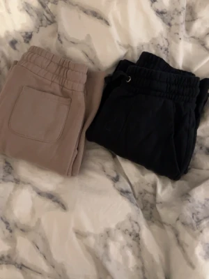 Bruna och svarta mjukisbyxor - Två par mjukisbyxor i brun och svart med resår i midjan och fickor framtill. Perfekta för chill dagar hemma eller när du vill vara bekväm. Klassisk passform och mjukt material som känns skönt mot huden.