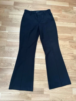 Svarta utsvängda kostymbyxor - Svarta kostymbyxor med utsvängda ben och klassiska pressveck. Byxorna har hällor för skärp och diskreta fickor.