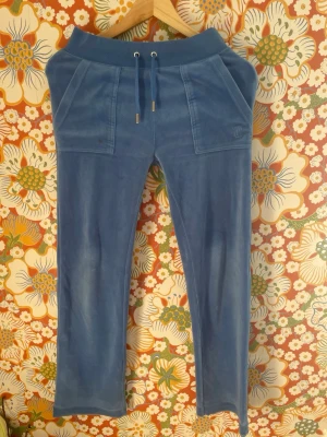 Blå velour mjukisbyxor med fickor - Säljer ett par blå mjukisbyxor i mjuk velour med bred resår i midjan och dragsko. Byxorna har stora framfickor och bakfickor med knappdetaljer. Perfekta för chill dagar och riktigt sköna att ha på sig.