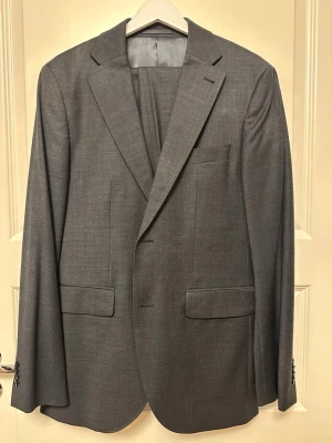 Kostym från Riley - Komplett mörkgrå kostym från Riley. Kavajen size 48, byxorna size 50