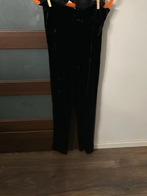 Svarta sammetsleggings - Säljer ett par svarta leggings i mjuk sammet med hög midja och smal passform. Perfekta för dig som vill ha något både bekvämt och snyggt. Materialet ger en lyxig känsla och de är stretchiga för bästa komfort.