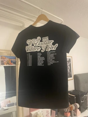Svart Hov1 t-shirt med tryck - Säljer en svart t-shirt från Hov1 med turnétryck 'Vi Dansar Vidare I Livet' på ryggen och en liten krona på bröstet. T-shirten har korta ärmar och rund hals. Perfekt för dig som gillar svensk musik och vill ha en stilren merch-tröja. Däremot är Hov1 loggan inuti på sista bilden bort klippt då jag tyckte den kliade för mycket! Pris kan diskuteras vid snabb affär!❣️