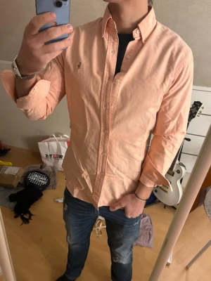 Ljus rosa skjorta från Ralph Lauren - Säljer en ljus rosa skjorta från Ralph Lauren med klassisk button-down krage och broderad logga på bröstet. Skjortan har lång ärm, normal passform och är tillverkad i mjuk bomull. Perfekt för en clean och stilren look.