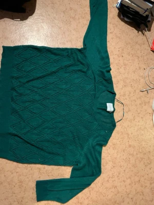 Grön stickad tröja från Junarose - Grön stickad tröja från Junarose med rund halsringning och långa ärmar. Tröjan har ett diskret diamantmönster över hela plagget och är perfekt för dig som gillar en enkel men snygg look.