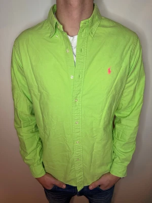 Grön skjorta från Ralph Lauren - Snygg limegrön skjorta från Ralph Lauren med klassisk button-down krage och rosa broderad logga på bröstet. Skjortan har långa ärmar och knäppning framtill. Perfekt för dig som vill sticka ut med färg! Storlek M och i extremt bra skick! Endast 245kr💙 // studio II Resell 💯