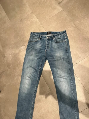 Blå jeans från Neuw - Säljer ett par klassiska blå jeans från Neuw med fem fickor och snygg tvättad look. Jeansen har normal midja, raka ben och kontrastsömmar. Perfekta till sneakers eller boots och passar till många olika stilar.