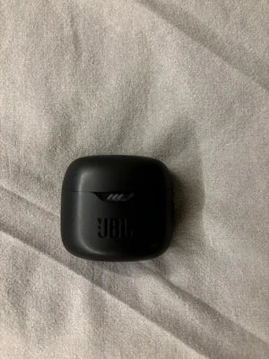 JBL hörlurar  - Säljer ett par svarta trådlösa in-ear hörlurar från JBL, modell Tune. Kommer i ett smidigt, matt svart laddningsetui med rundade kanter och JBL-logga på framsidan. Perfekta för musik, poddar och samtal när du är på språng. Dem har också noise canceling