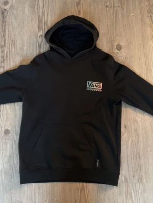 Svart hoodie från Vans med tryck - Svart hoodie från Vans. Stor färgglad 'Off The Wall Vans'-grafik på ryggen. Mjuk bomullsmix, huva och stor magficka framtill. Hoodien är som en XS men L i barnstorlek 💕