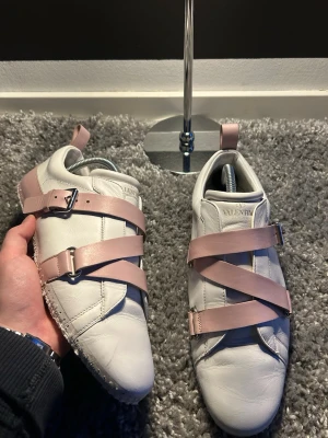 Valentino vita sneakers med rosa band(utan yttersula) - Unika vita sneakers från Valentino med breda, ljusrosa band och spännen över foten. Skorna är låga och har en modern design med detaljer i metall. Tillverkade i mjukt läder för en exklusiv känsla. Perfekta för dig som vill sticka ut med din stil.byten kan vara intressant och priset kan diskuteras!! Skriv vid minsta lilla fråga!!
