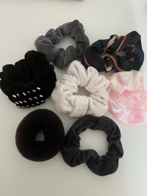 scrunchies - Säljer ett set med sex scrunchies i olika färger och material. Inkluderar svart med pärlor, vit med pärlor, grå sammet, svart sammet, svart med orange rand, rosa skimrande och en hår balett boll. Perfekt för att variera din look och matcha olika outfits.