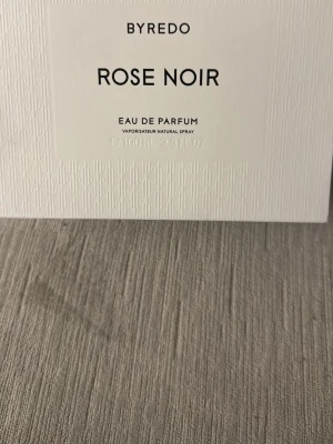 Byredo Rose Noir Eau de Parfum - Byredo Rose Noir Eau de Parfum i elegant glasflaska med svart lock och vit etikett. Doften är exklusiv och modern med tydlig ros-karaktär. Flaskan rymmer 100 ml och kommer i en stilren vit förpackning med präglat mönster.
