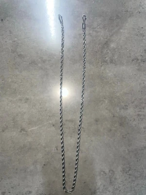 Silverfärgat tvinnat halsband - Snyggt halsband i silverfärg med tvinnad kedja och karbinhake. Halsbandet har en enkel men stilren design som passar till många olika looks. Materialet ser ut att vara metall och kedjan har en diskret glans.