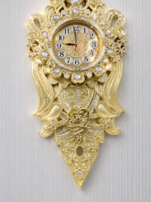 Dekorativ guldig väggklocka - Unik och lyxig väggklocka i guld med detaljerade utsmyckningar och gnistrande stenar runt urtavlan. Klockan har en klassisk rund form och är prydd med pärlliknande dekorationer och ornamenterade mönster. Perfekt för dig som vill ha något extra i rummet.