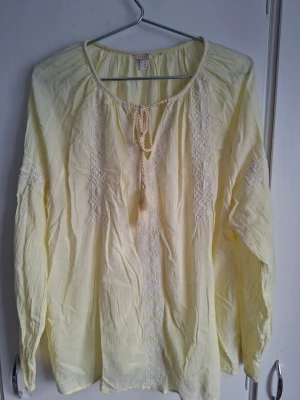 Gul blus från Esprit - Ljusgul blus från Esprit med långa ärmar och broderade detaljer framtill och på ärmarna. Blusen har en rund halsringning med knytband och är tillverkad i ett lätt, luftigt tyg som ger en avslappnad känsla.
