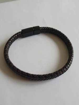 LÄDERARMBAND - FLÄTAT - Snyggt armband i mörkbrunt flätat läder med ett stilrent svart magnetlås. Perfekt accessoar för dig som gillar en enkel men trendig look. Passar både till jeans och skjorta och ger en cool touch till din outfit.