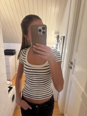 Randig croppad topp med rund hals - Snygg vit och svart randig topp med croppad passform och rund, djup ringning. Kortärmad modell i mjukt material som sitter tight och framhäver figuren. 