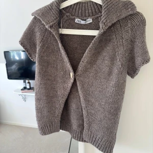 Brun stickad kofta från Zara - Säljer en brun stickad kofta från Zara med korta ärmar och stor krage. Koftan har en knapp framtill och är perfekt att slänga över en topp eller klänning nu i sommar. 