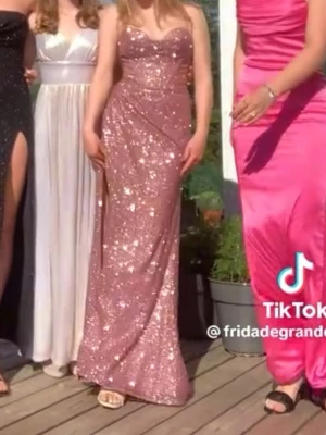 Rosa balklänning  - Säljer en glittrig rosa balklänning med fin snörning baktill och slits på ena sidan. Klänningen har figurnära passform och är axelbandslös, perfekt för bal eller fest. Materialet är glittrigt och skimrande, perfekt i soligt väder!