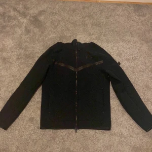 Svart fleecejacka från Nike - Säljer en svart fleecejacka från Nike med dragkedja framtill. Jackan har en stilren design med långa ärmar och hög krage. Perfekt för kyliga dagar.