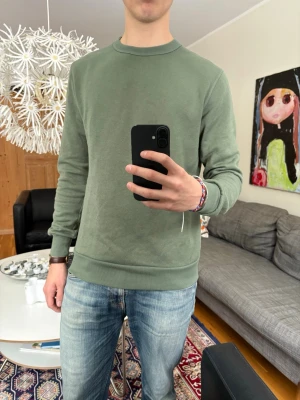 Grön crewneck sweatshirt - Säljer en stilren grön crewneck sweatshirt med rund halsringning och ribbade muddar vid ärmslut och nederkant. Materialet känns mjukt och bekvämt mot huden.