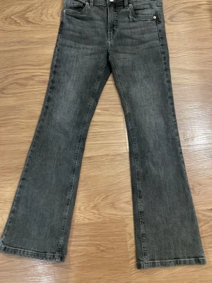 Gråa bootcut jeans - Säljer ett par gråa bootcut jeans med klassisk femficksdesign och normal midja. Jeansen har en lätt tvättad look och vida ben från knät och ner. Perfekta för dig som gillar retrostil och vill ha ett par bekväma jeans med snygg passform.