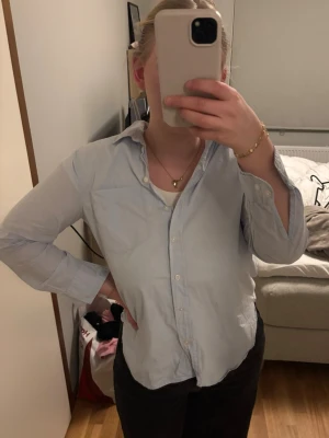 Ljusblå skjorta från H&M - Klassisk ljusblå skjorta från H&M i bomull. Skjortan har krage, knappar framtill och en bröstficka. Perfekt till jeans eller kjol för en clean och enkel look. Man kan ha armarna både öppna och stängda. Säljer då den inte kommer till användning, endast använd någon enstaka gång. storlek S💙
