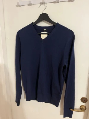 Mörkblå V-ringad tröja från Uniqlo - Snygg mörkblå stickad tröja från Uniqlo med V-ringning. Tillverkad i extra fin merinoull som känns mjuk och lätt på kroppen. Klassisk passform med långa ärmar och ribbade muddar. Perfekt att matcha med jeans eller skjorta. Oanvänd!