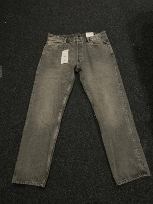 Grå raka jeans från Jack&Jones - Säljer ett par helt nya och oanvända grå jeans från Jack&Jones med rak passform och klassisk femficksdesign. Jeansen har en snygg tvättad look och är tillverkade i kraftigt denimtyg. 