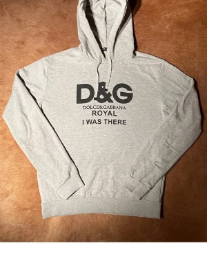 Dolce & Gabbana Hoodie - Snygg grå hoodie från Dolce & Gabbana med stor svart D&G-logga och texten 'ROYAL I WAS THERE' på bröstet. Klassisk modell med huva och ribbade muddar vid ärmar och nederkant. Perfekt för en avslappnad och trendig look.