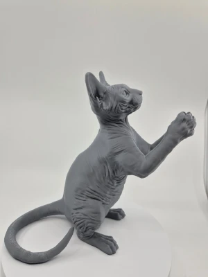 Grå statyett av sphynxkatt lampa - Detaljerad statyett föreställande en sphynxkatt i sittande position med framtassarna upphöjda för att hålla i en lampsockel. Figuren är grå och har tydliga veck och textur som liknar kattens hud. 