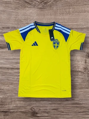 Sverige matchtröja Adidas gul/blå - Säljer en officiell Sverige matchtröja från Adidas i starkt gul med blå detaljer och vita ränder på axlarna. Tröjan har rund hals, korta ärmar och det svenska landslagets emblem på bröstet. Tillverkad i lätt och ventilerande material.