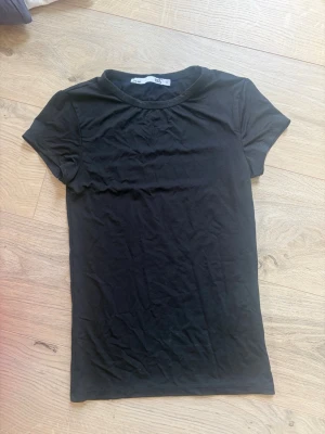 Svart basic t-shirt från 157 S - En enkel svart t-shirt från 157 med rund hals och korta ärmar. Tillverkad i mjuk bomull som känns skön mot huden. Perfekt att matcha med jeans eller shorts för en clean och stilren look.