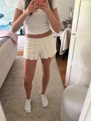 Vita stickade shorts med volangkant - Säljer ett par vita stickade shorts med snygg volangkant och ribbad midja. De är högmidjade och har ett unikt mönster som ger en cool och trendig look. Perfekta för sommarens chill dagar och passar dig som gillar en avslappnad stil.