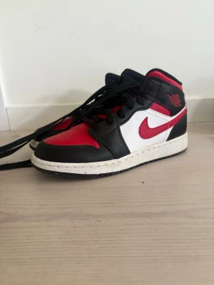 Nike Air Jordan  röd/svart/vit - Snygga Nike Air Jordan  sneakers i klassiska färger: rött, svart och vitt. Skorna har en ikonisk siluett med svart läder, röda detaljer och vit panel samt den röda swoosh-loggan på sidan. Perfekta för dig som gillar streetwear och vill sticka ut.