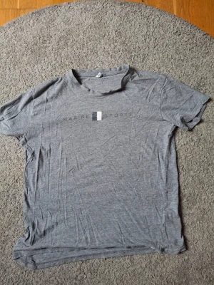 Grå t-shirt från Marine Sports - Säljer en grå t-shirt från Marine Sports med diskret logga på bröstet. T-shirten har klassisk rund hals och korta ärmar, perfekt för en chill och avslappnad look. Materialet är mjukt och känns som bomull, vilket gör den riktigt bekväm.