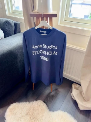 Blå långärmad Acne Studios tröja - Snygg blå långärmad topp från Acne Studios med vit text framtill där det står 'Acne Studios STOCKHOLM 1996'. Enormt bra skick!!😁