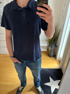 Mörkblå frottéskjorta från Les Deux - Säljer en mörkblå skjorta från Les Deux i mjuk frotté. Skjortan har korta ärmar, klassisk krage och knappar vid halsen. Perfekt för en avslappnad och cool stil. Passformen är normal och materialet känns riktigt bekvämt.
