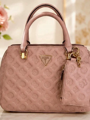 Rosa handväska från Guess - Snygg ljusrosa handväska från Guess med quiltat mönster och guldfärgade detaljer. Väskan har dubbla handtag, en avtagbar liten väska framtill och en praktisk ytterficka med dragkedja på baksidan. Tillverkad i konstläder med Guess-logga framtill.