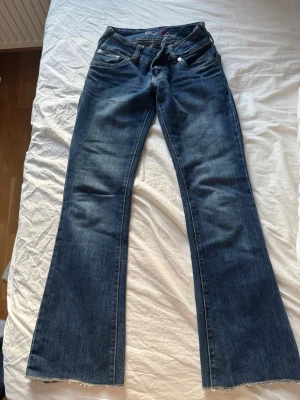Blå bootcut jeans med döskalle - Säljer ett par blå bootcut jeans med rå kant och döskallebrodyr på bakfickorna. Jeansen har klassisk femficksmodell och låg midja. Perfekta för dig som gillar en edgy stil.